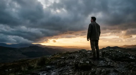 A person standing at the edge of a storm cloud looking toward distant sunlight breaking through, symbolizing realistic hope during crisis