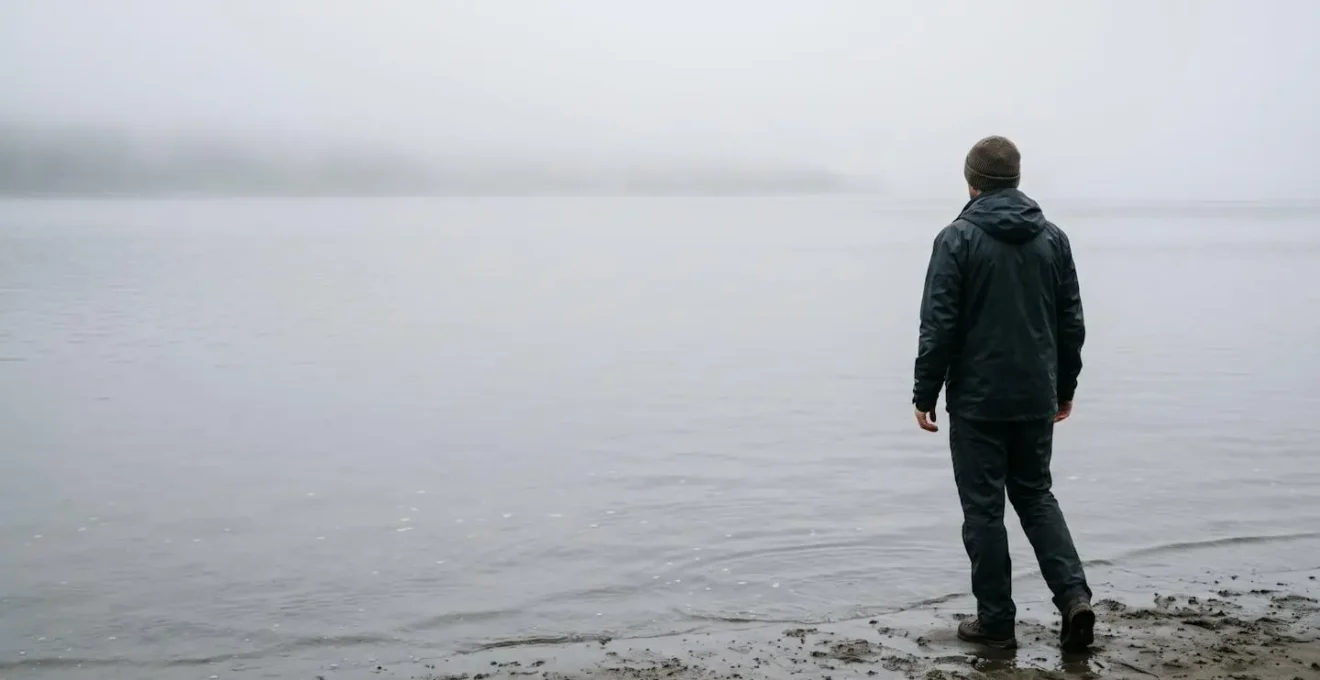 A person stands at the edge of the water looking towards a misty horizon, symbolizing the balance between the comfort zone and the growth zone.