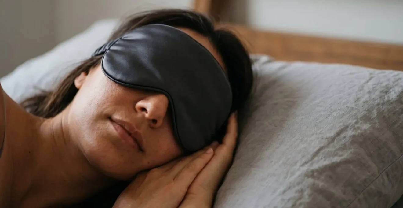 Peaceful close-up of person wearing contoured silk sleep mask in serene bedroom environment