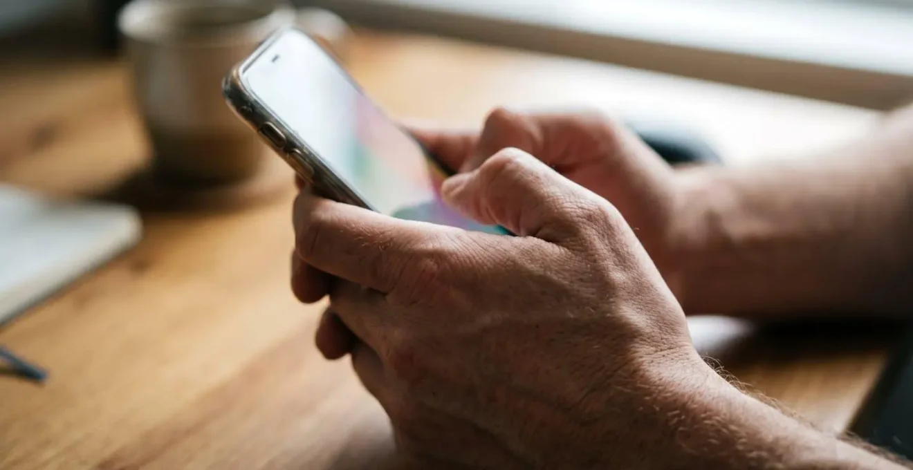 A professional's hands tensed while scrolling through a smartphone, symbolizing the anxiety of social comparison at work.